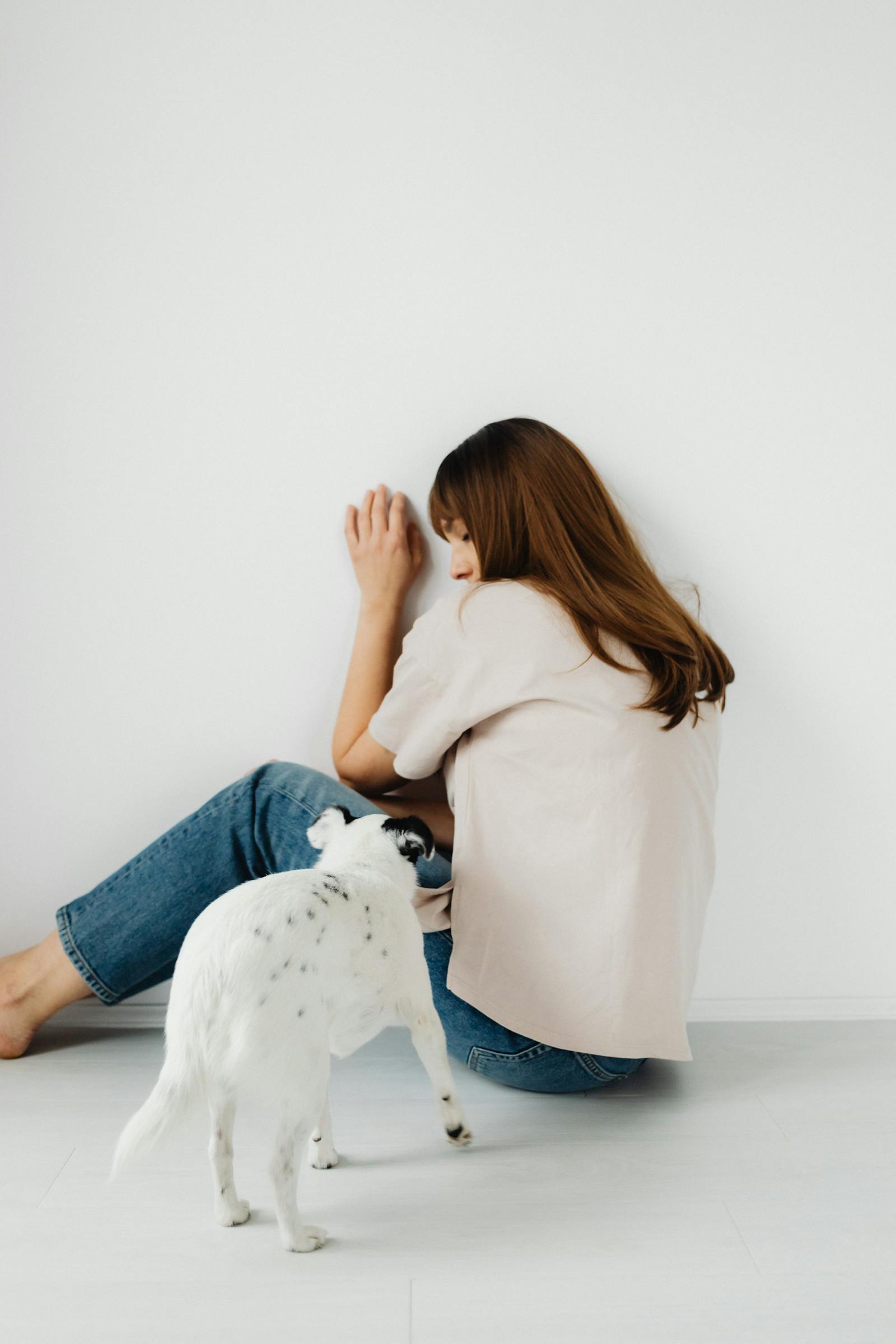 Vrouw zit op de grond tegen een muur en troost haar witte hond — beeld van angst en geruststelling